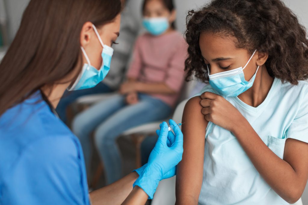 Kids Vaccination. Nurse Vaccinating Black Preteen Girl Injecting Vaccine Against Covid-19 With Syringe Indoors. Child Getting Vaccinated For Immunization In Modern Clinic. Selective Focus